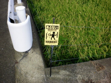 あぶない!と書かれた看板と電気柵が畑に設置されている写真