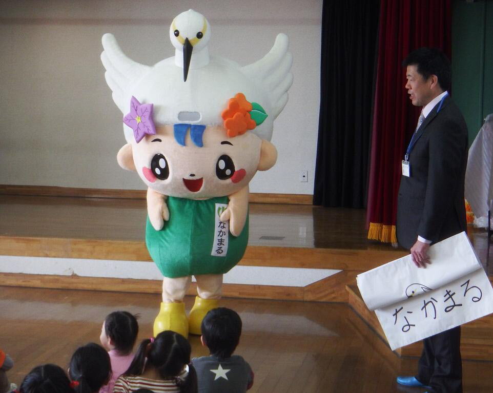 子供たちの前に、ゆるキャラ「なかまる」が立っている横に、なかまると書かれた模造紙を持っているスーツ姿の男性の写真