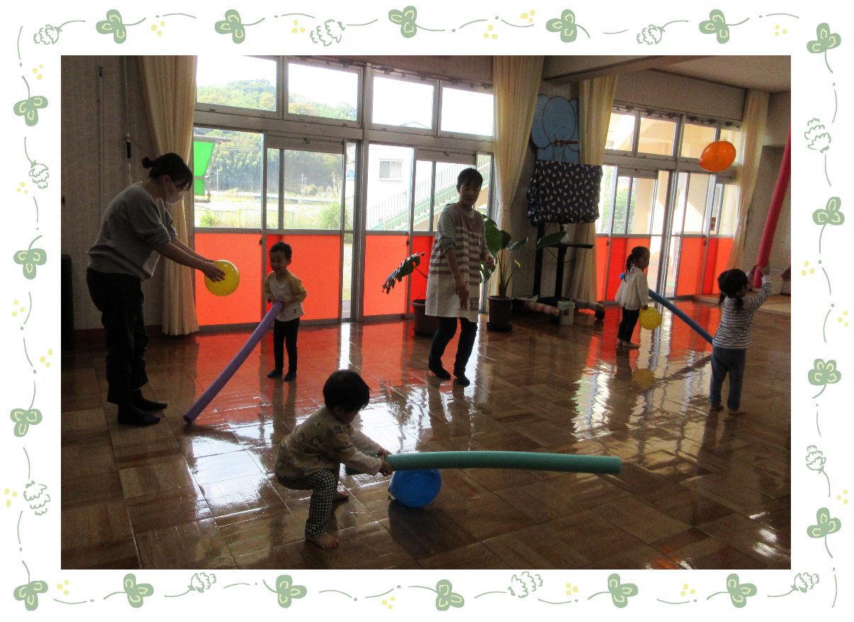 ホールでスポンジの棒を使い風船を飛ばしている子どもたち