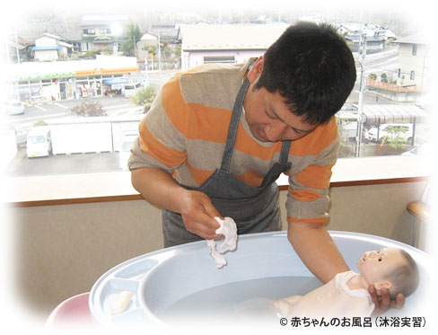 赤ちゃんのマネキンを使ってお風呂の入れ方を学んでいるお父さんの写真(C) 赤ちゃんのお風呂（沐浴実習）