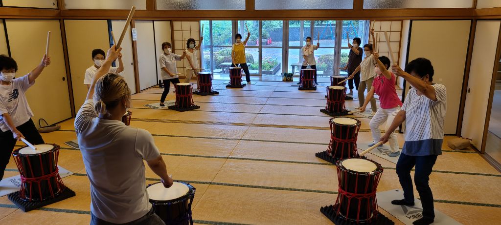 講師と参加者が立位で力強く和太鼓を叩くバチを振り下ろす様子