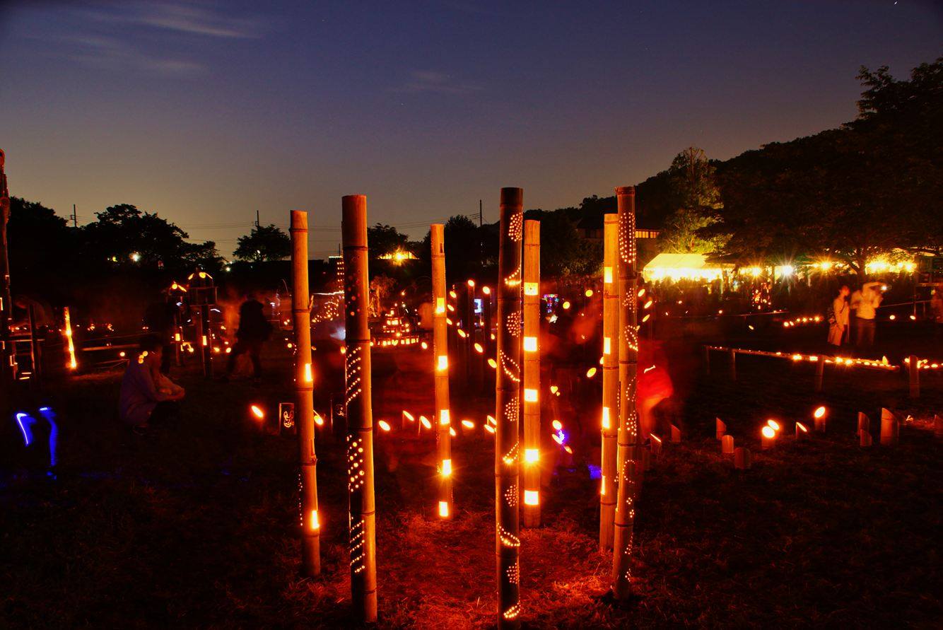 等間隔に光る長い竹の灯篭が円状に並べて立てられている写真