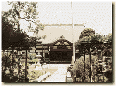 米倉寺まで続く道の両側に木々が植えられ正面に瓦屋根の米倉寺がある白黒写真