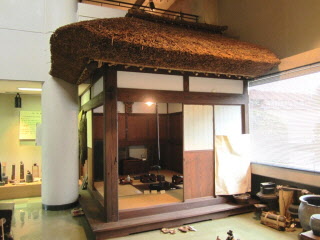 藁ぶき屋根で囲炉裏のある畳の部屋が再現されている農家の居室の写真