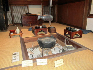 畳の部屋の中央に正方形の囲炉裏があり、鉄なべが置かれ、食器の並んだお膳が置かれている写真
