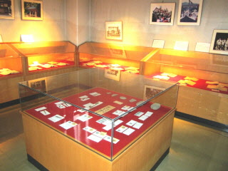 出土品が入った展示ケースが中央に一か所、壁に沿って配置されており、壁にも写真が展示されている展示室内の写真