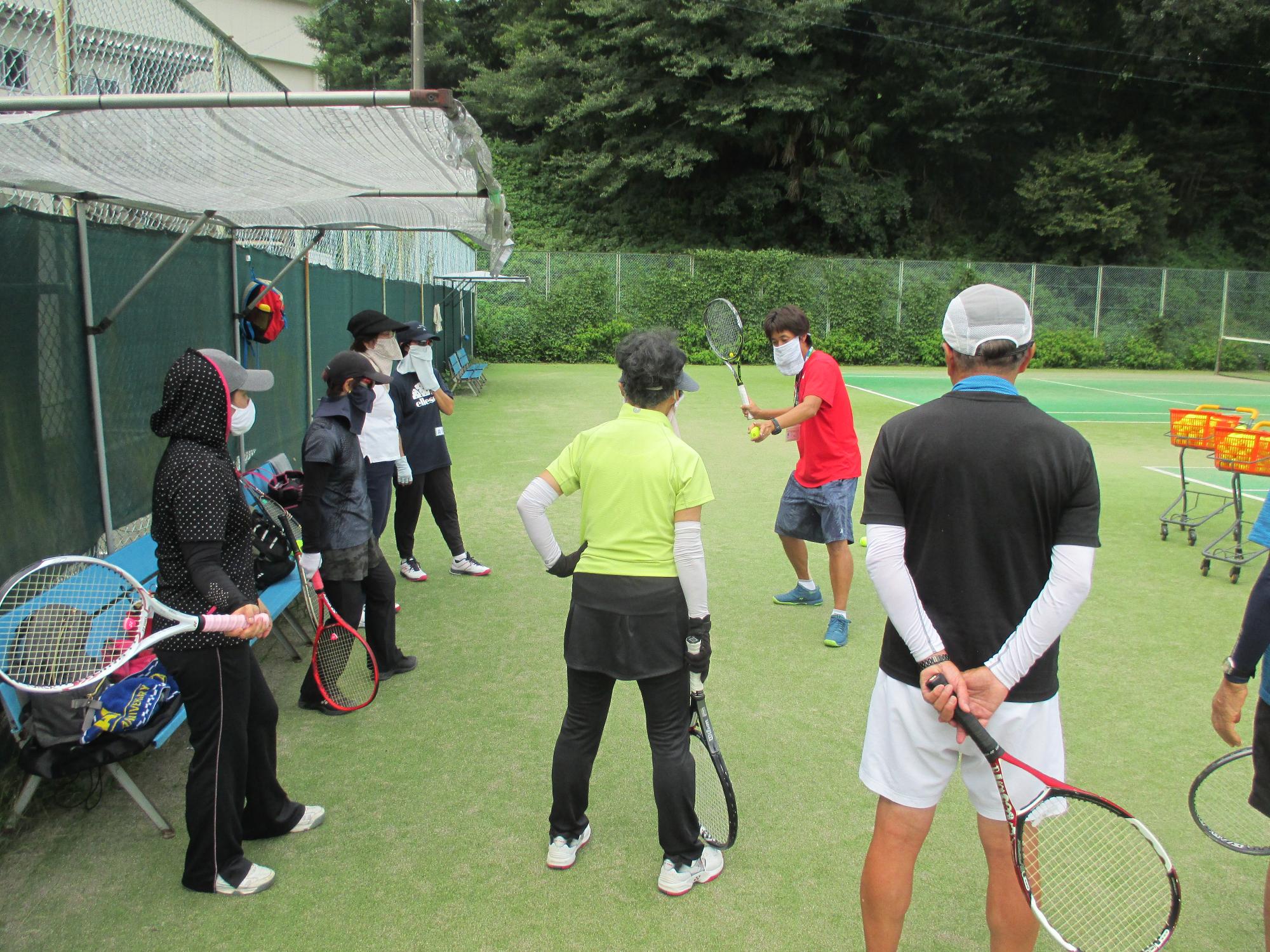 テニス教室でコーチが参加者に指導をしている写真