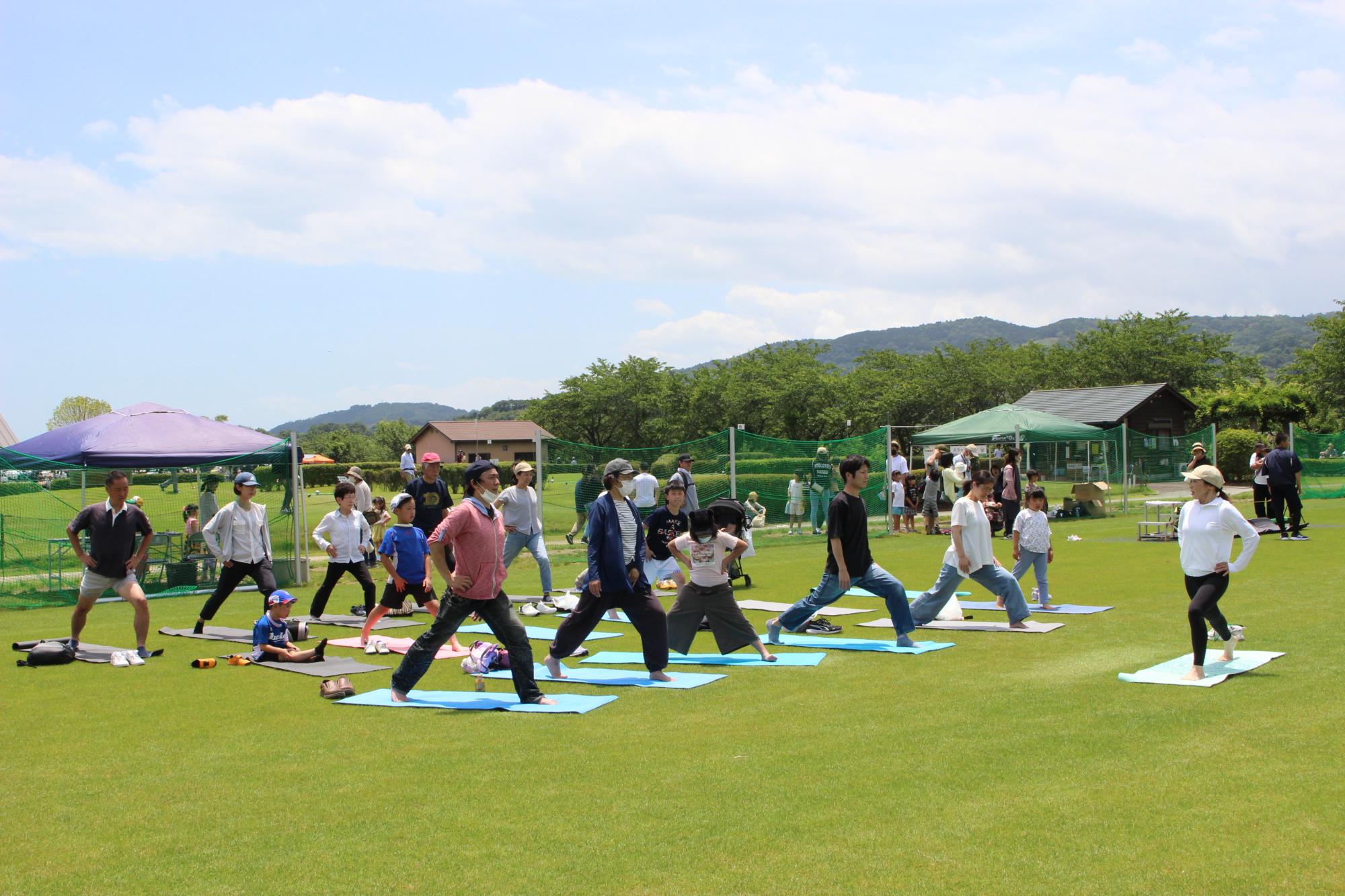 スポレク祭で芝生の上で20人の男女がヨガをやっているところ