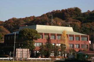 後方には山々があり、屋根部分が白色で茶色い外壁の中井町役場の写真
