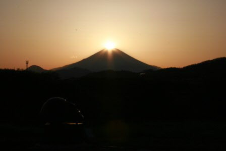 富士山頂に太陽が重なってオレンジ色に輝いている写真